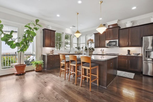 kitchen featuring light stone counters, stainless steel appliances, a breakfast bar, a kitchen island, and decorative light fixtures