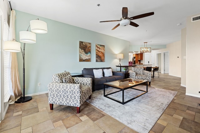 living room featuring ceiling fan with notable chandelier, stone finish floor, and baseboards