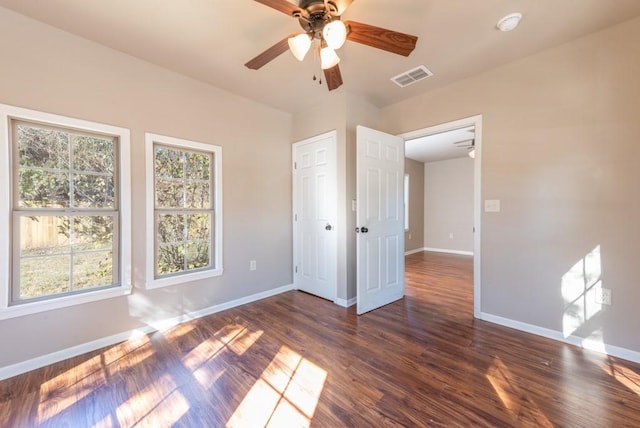 empty room with a ceiling fan, visible vents, dark wood finished floors, and baseboards