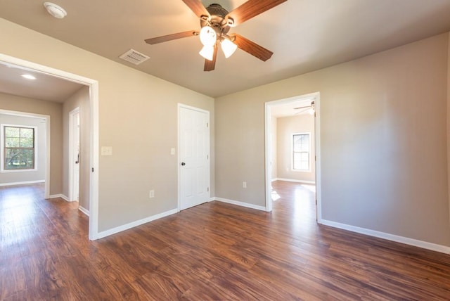 empty room featuring a healthy amount of sunlight, baseboards, visible vents, and dark wood finished floors