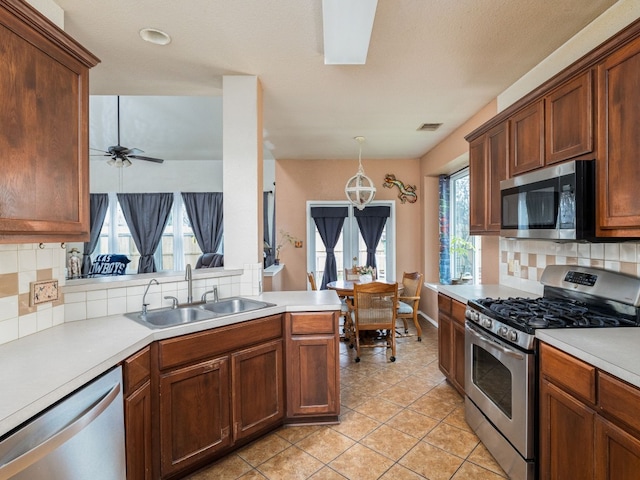 kitchen with a sink, light countertops, appliances with stainless steel finishes, hanging light fixtures, and tasteful backsplash