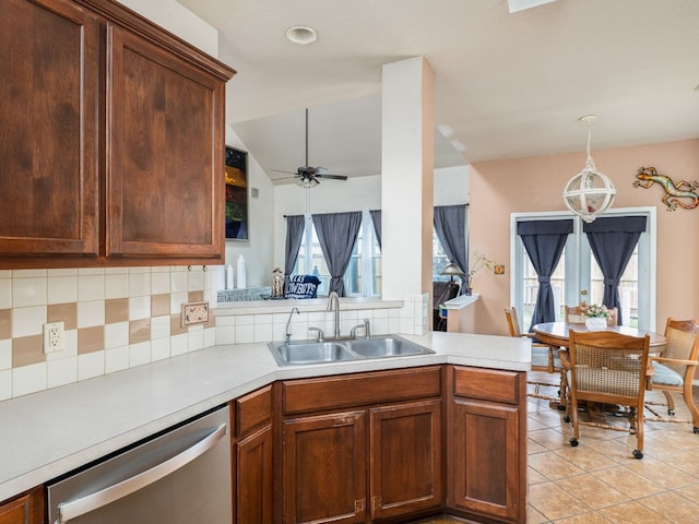 kitchen featuring a peninsula, a sink, light countertops, dishwasher, and decorative light fixtures