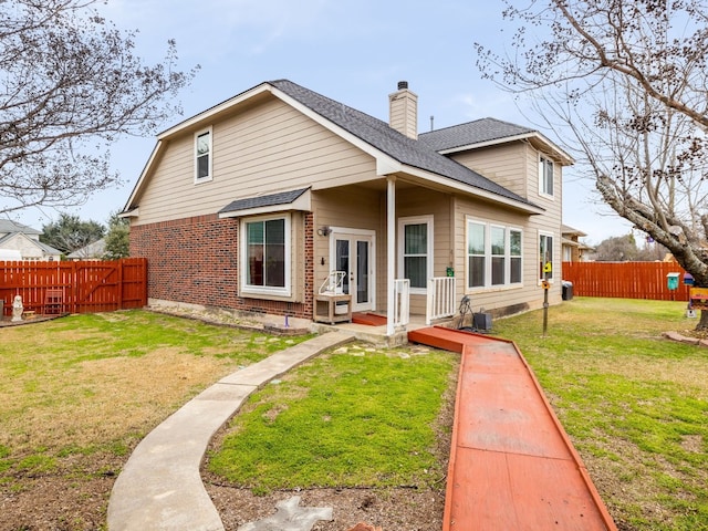 rear view of house featuring a yard, a fenced backyard, a chimney, and brick siding