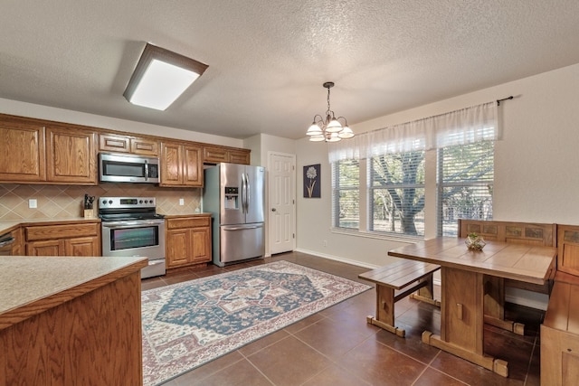 kitchen with decorative light fixtures, light countertops, decorative backsplash, appliances with stainless steel finishes, and brown cabinetry