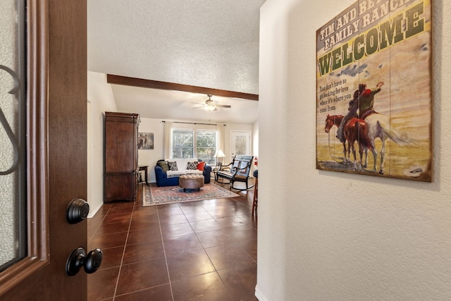 hallway featuring a textured wall, baseboards, a textured ceiling, and dark tile patterned flooring