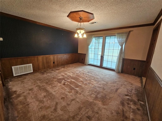 carpeted spare room featuring a wainscoted wall, visible vents, a textured ceiling, and ornamental molding