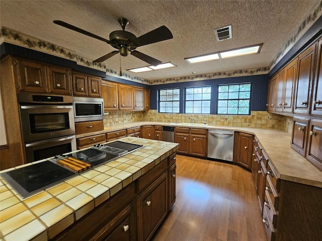 3105 Indian Mound Rd, Georgetown, TX 78628 - kitchen featuring appliances with stainless steel finishes, tile countertops, wood finished floors, ceiling fan, and decorative backsplash