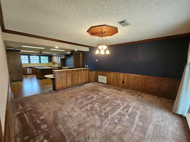 kitchen featuring visible vents, hanging light fixtures, brown cabinetry, wainscoting, and a peninsula