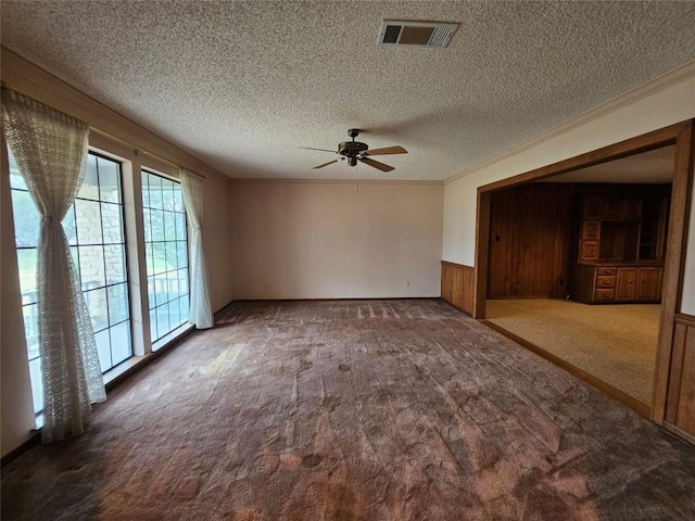 spare room with ornamental molding, dark colored carpet, a wainscoted wall, and visible vents