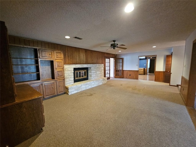 3105 Indian Mound Rd, Georgetown, TX 78628 - unfurnished living room featuring wooden walls, ceiling fan, light carpet, a textured ceiling, and a stone fireplace
