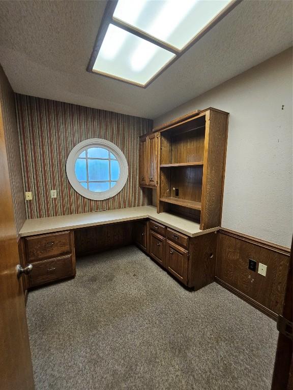 unfurnished office featuring a wainscoted wall, carpet, a textured ceiling, and built in study area