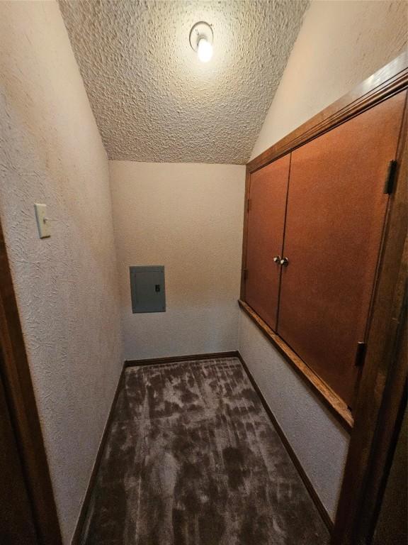 hallway featuring a textured wall, vaulted ceiling, a textured ceiling, and dark colored carpet