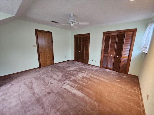 unfurnished bedroom featuring multiple closets, visible vents, a textured ceiling, and carpet floors