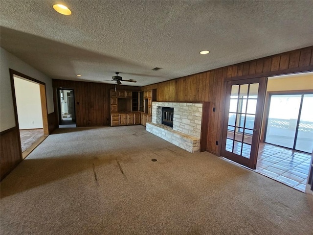 3105 Indian Mound Rd, Georgetown, TX 78628 - unfurnished living room featuring wood walls, carpet flooring, a ceiling fan, a textured ceiling, and a fireplace
