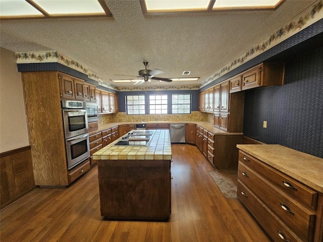 kitchen with appliances with stainless steel finishes, a center island, tile countertops, and dark wood-style floors