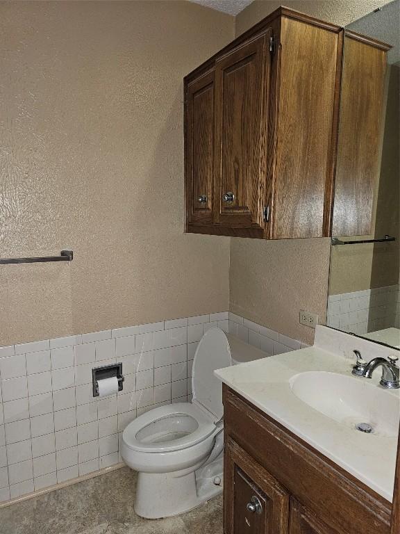 bathroom with a wainscoted wall, tile walls, a textured wall, toilet, and vanity