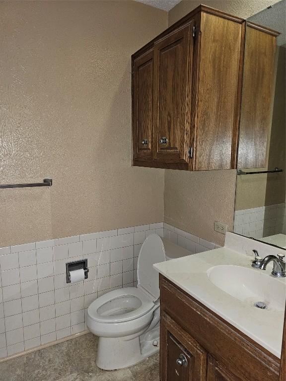 3105 Indian Mound Rd, Georgetown, TX 78628 - half bathroom with vanity, a textured wall, toilet, tile walls, and a wainscoted wall
