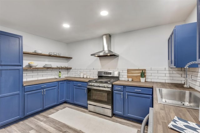 kitchen with butcher block countertops, stainless steel gas range, blue cabinets, and wall chimney range hood