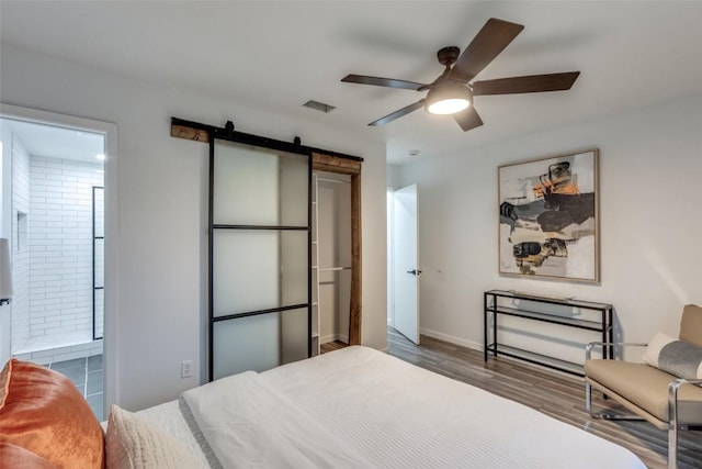 bedroom featuring ceiling fan, a barn door, wood finished floors, visible vents, and ensuite bath