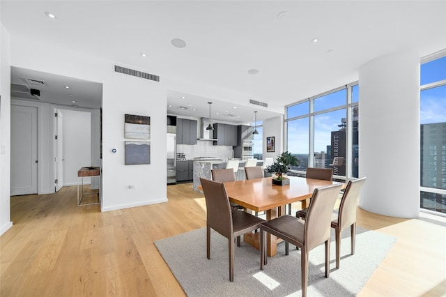 dining space featuring visible vents, baseboards, light wood-style flooring, a view of city, and floor to ceiling windows