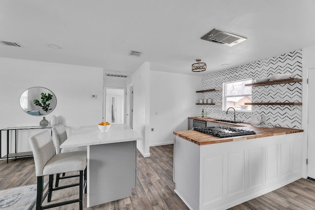 kitchen with a breakfast bar area, open shelves, visible vents, a sink, and butcher block countertops