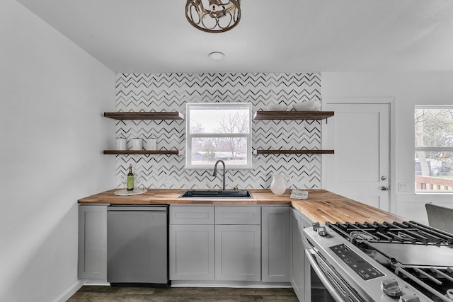 kitchen with decorative backsplash, butcher block countertops, appliances with stainless steel finishes, open shelves, and a sink