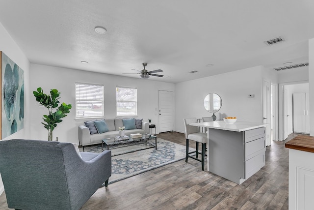 living room with a ceiling fan, visible vents, and wood finished floors