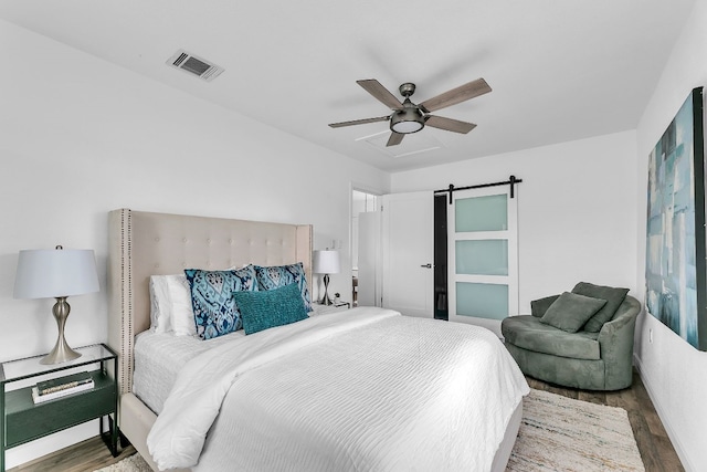 bedroom with a ceiling fan, wood finished floors, visible vents, and a barn door