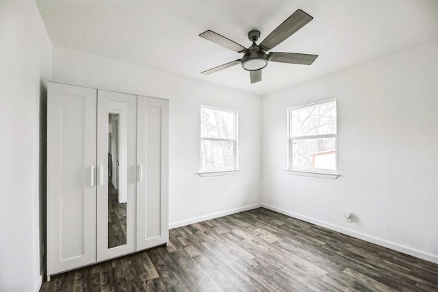 unfurnished bedroom featuring dark wood-style flooring, a closet, a ceiling fan, and baseboards