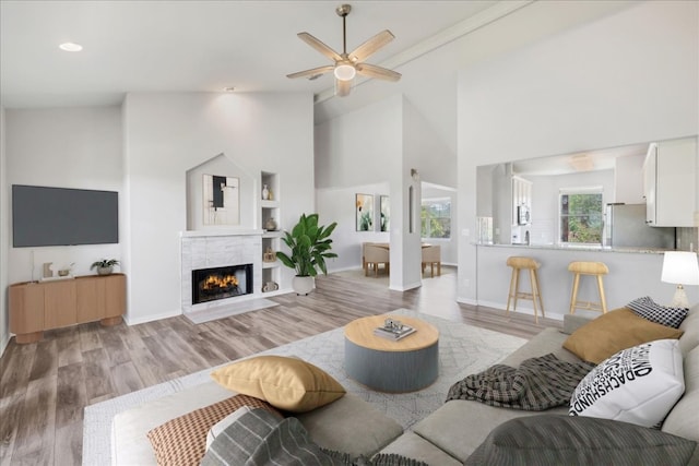 living area with a fireplace with flush hearth, a ceiling fan, baseboards, and wood finished floors