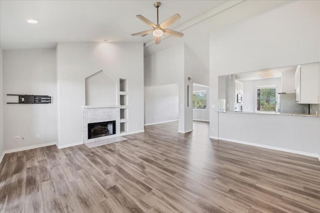 unfurnished living room featuring a fireplace with flush hearth, wood finished floors, baseboards, and a ceiling fan