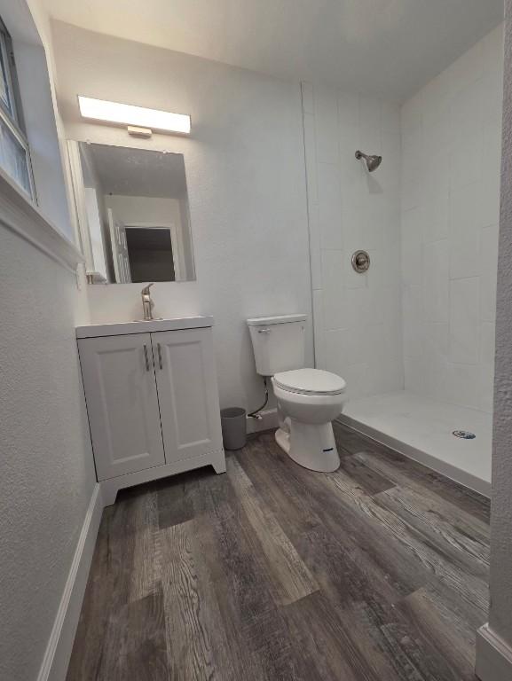 full bathroom with a tile shower, vanity, toilet, and wood finished floors