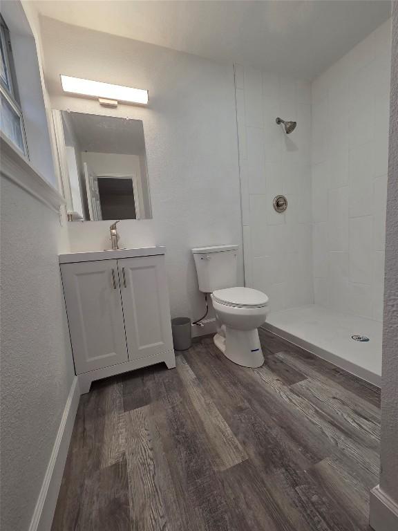 bathroom with toilet, tiled shower, and wood finished floors