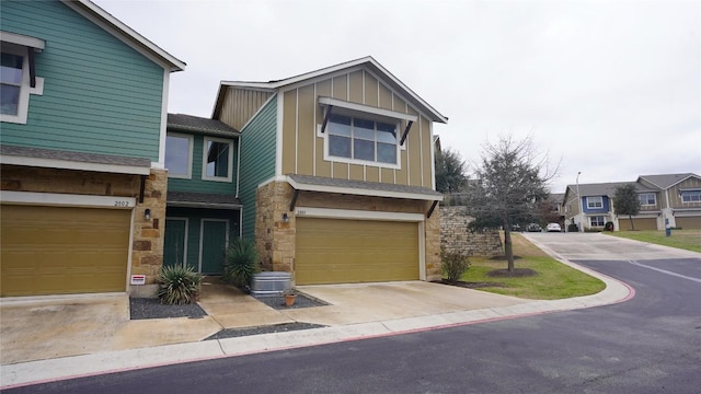 multi unit property with board and batten siding, stone siding, driveway, and an attached garage