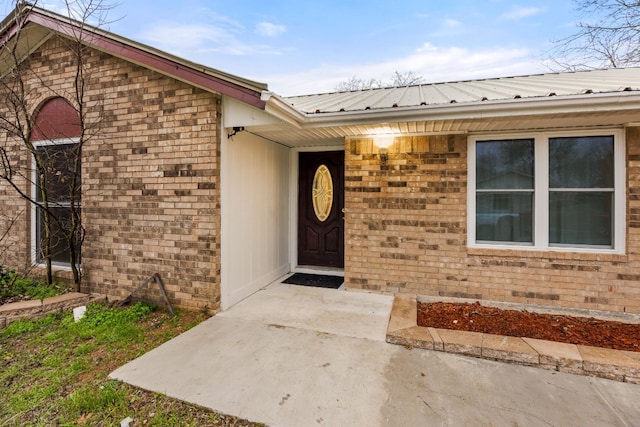 entrance to property featuring a patio area, metal roof, and brick siding