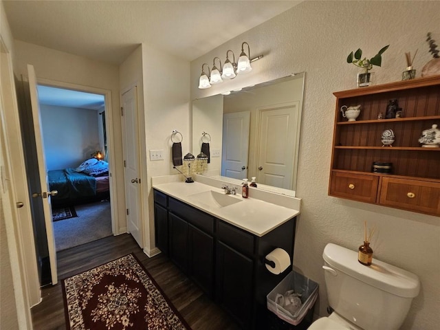 bathroom with toilet, a textured wall, wood finished floors, and vanity