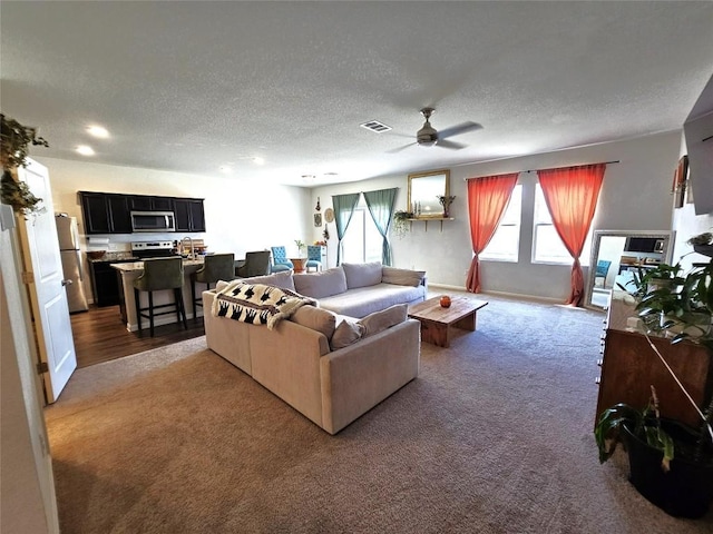 carpeted living room featuring visible vents, a ceiling fan, and a textured ceiling