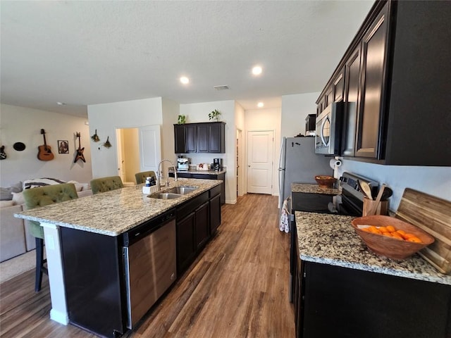 kitchen featuring visible vents, appliances with stainless steel finishes, dark wood-type flooring, a sink, and an island with sink