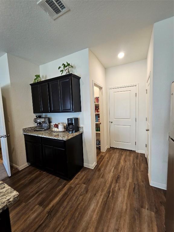 kitchen featuring dark cabinets, visible vents, baseboards, light stone countertops, and dark wood-style floors