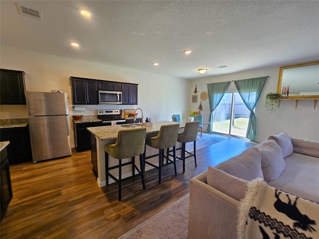 kitchen with a center island with sink, dark wood finished floors, appliances with stainless steel finishes, open floor plan, and a kitchen bar