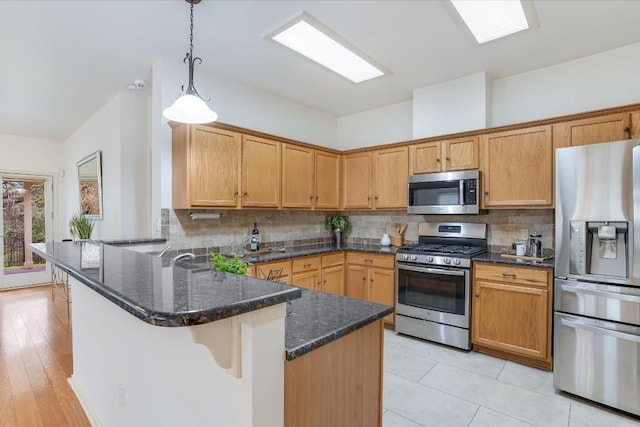 kitchen featuring decorative light fixtures, stainless steel appliances, backsplash, dark stone countertops, and a peninsula