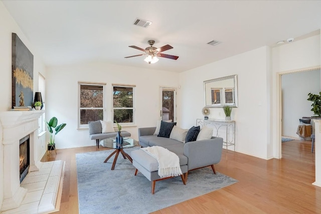 living room with ceiling fan, light wood-style flooring, a tile fireplace, and visible vents