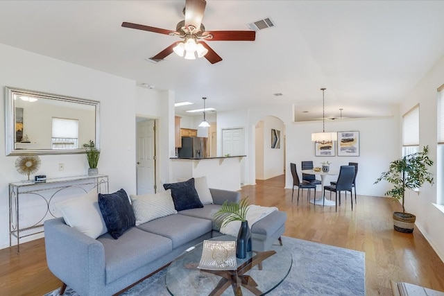 living area featuring arched walkways, visible vents, ceiling fan, and wood finished floors