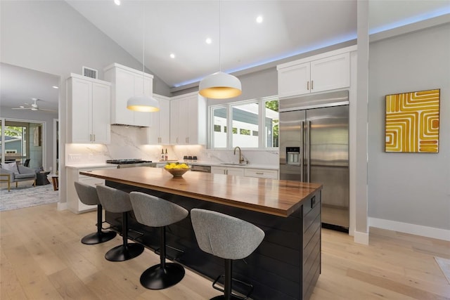 kitchen featuring stainless steel appliances, wood counters, white cabinetry, a center island, and pendant lighting