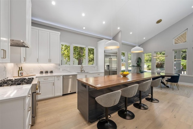 kitchen featuring a sink, high quality appliances, white cabinetry, a center island, and decorative light fixtures