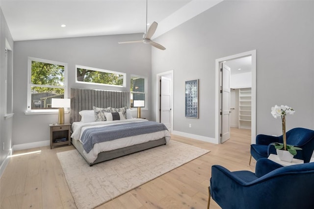 bedroom with a walk in closet, light wood-style flooring, ceiling fan, high vaulted ceiling, and baseboards