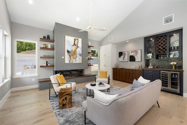 living room with visible vents, wine cooler, wet bar, light wood-type flooring, and high vaulted ceiling