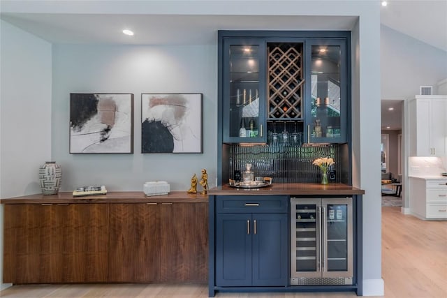 bar featuring light wood-style flooring, beverage cooler, visible vents, backsplash, and a bar