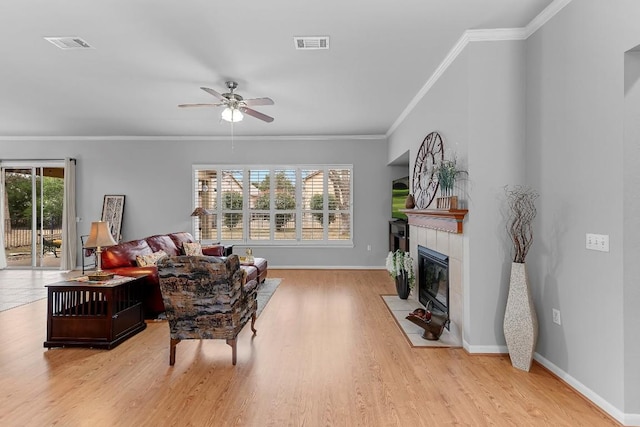 living room with a fireplace, light wood finished floors, visible vents, ornamental molding, and baseboards