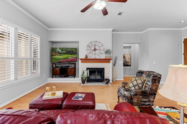 living area with visible vents, a ceiling fan, a tiled fireplace, ornamental molding, and wood finished floors